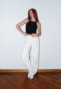 Czarny bezrękawnik crop top i białe spodnie z wysokim stanem i szerokimi nogawkami. Modelka stoi na tle gładkiej ściany, prezentując casualowy, nowoczesny strój.