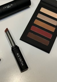 Pomadka L'Oréal w czarnym opakowaniu; obok paleta do cieni do powiek w czarnym kolorze z pięcioma odcieniami: beżowym, błyszczącym brązem, średnim brązem, czerwonym, ciemnym brązem.