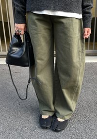 Oljčno zelene široke hlače, sivi pleteni pulover, črna usnjena torbica z dolgim trakom in črni čevlji z razporkom na prstih. Teksturirani in sproščen kroj.