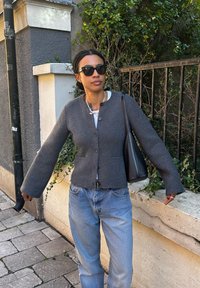 Γκρίζα πουλόβερ από μάλλινο ύφασμα με στρογγυλή λαιμόκοψη, κλείσιμο με κουμπιά και φαρδιά μανίκια. Συνδυασμένο με ανοιχτόμπλε τζιν και μαύρη τσάντα ώμου.