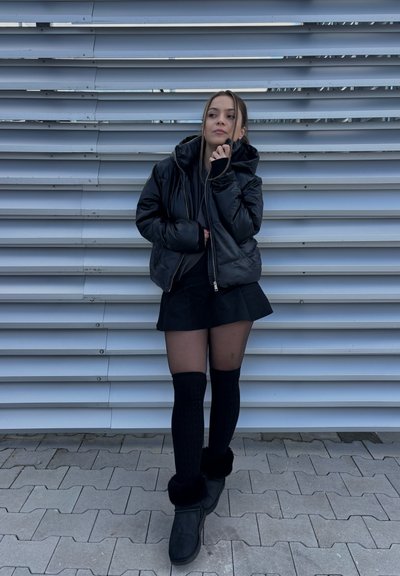 Chaqueta negra acolchada con capucha, sobre una camiseta negra. Falda negra, medias transparentes, calcetas negras hasta la rodilla y botines negros con borde de piel. 