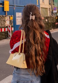 Geantă galbenă din piele lacuită cu design structurat și accente argintii, purtată cu un top roșu cu model și pantaloni scurți din denim, părul aranjat cu o agrafă.