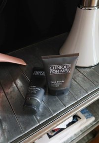 Esfoliante per il viso Clinique for Men e idratante oil-free, entrambi in tubi grigi. Superfici testurizzate con scritte bianche chiare, capacità di 100 ml ciascuno.