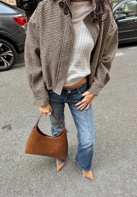 Jachetă maro cu model houndstooth, pulover alb din tricot cu fire, blugi, geantă din piele maro și pantofi cu vârf ascuțit nud pe o stradă pavata.