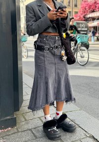 Črna denim krila z resicami na robu, v kombinaciji s črnim pasom s krožnimi dodatki. Črna puhasta obutev, bele nogavice z rdečim vzorcem srca.