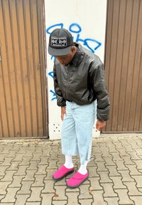 Zwarte leren bomberjack, lichtblauwe denim cropped broek, witte sokken en felroze klompen met zwarte zolen op een gestructureerde asfalt achtergrond.