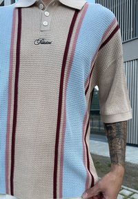Beige strik polo skjorte med horisontale striber i lyseblå, burgunder og pink. Tre-knaps placket og korte ærmer. Dekorativt logo detaljer.