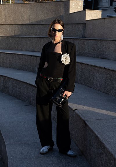 Blazer negro sobre un body con cortes, acento de flor plateada, pantalones anchos negros y zapatillas blancas. Accesorio: pequeña bolsa negra.