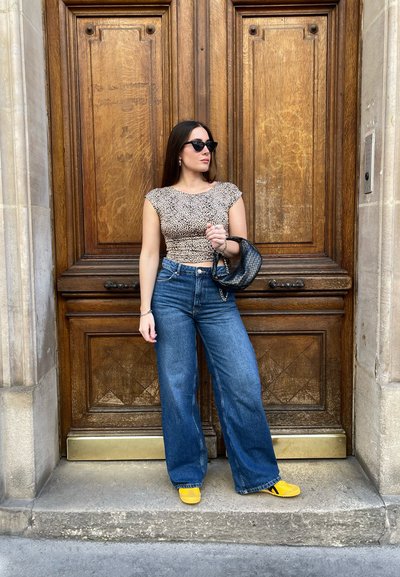 Top corto de estampado de leopardo, jeans de pierna ancha de tiro alto en azul y zapatos planos amarillos. Un bolso negro y gafas de sol completan el look.