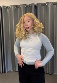 Haut à manches longues bleu clair côtelé avec silhouette ajustée, associé à un pantalon ample foncé. Le mannequin a des tresses bouclées blondes et un collier simple.