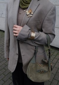 Beige teksturert blazer med oppbrettede ermer, grønn skulderveske i semsket skinn og en gullfarget blomsterbrosje. Under er en brun topp.