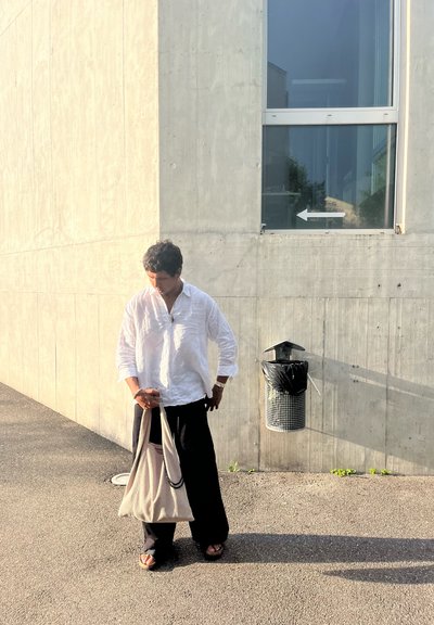 Bolso tote ligero en color beige con una tela texturizada y acentos en negro, combinado con pantalones negros holgados y una camisa blanca de botones.