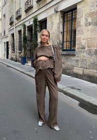 Brun krinklad tvådelad outfit med lång ärm, vida byxor och en lager-peplum topp; kompletterad med silverskor och en ljus väska.