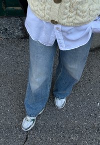 Jasnoniebieskie dżinsy o szerokim kroju z wyblednym wykończeniem, zestawione z białą koszulą na guziki i kremowym swetrem w warkocze. Białe i zielone sneakersy.