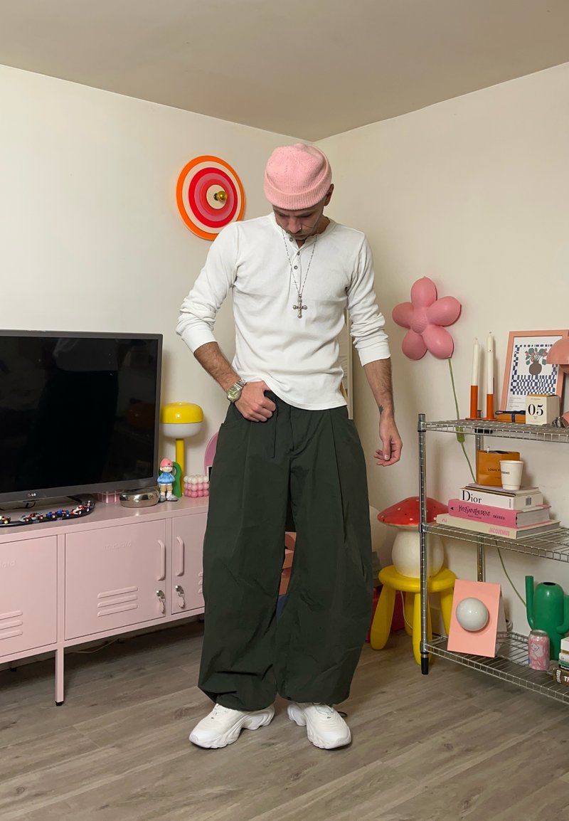 Camicia bianca a maniche lunghe, pantaloni verdi a gamba larga e scarpe da ginnastica bianche. Berretto rosa e gioielli d'argento. Decorazioni colorate sullo sfondo.