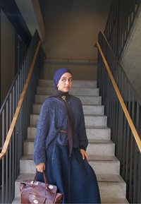 Pull en maille bleu marine avec un motif texturé, jupe longue en denim, sac à main marron et écharpe marron foncé. Debout sur des escaliers en béton.