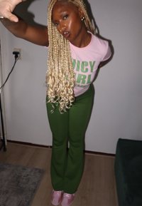 Camiseta rosa com o texto verde em negrito "JUICY GIRL", combinada com calças verdes e ténis rosas. Cabelo loiro longo e encaracolado e brincos de argola dourados.