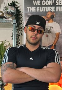 Must mustrella mustre, mustresse sini joosta, mustre peegli prillid oranžidega objektiividega, must kork ja nähtavad tätoveeringud. Taustal on taimed.