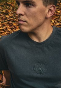 Graues Baumwoll-T-Shirt mit einem strukturierten Logo "Calvin Klein Jeans" auf der Vorderseite. Standard Rundhalsausschnitt und kurze Ärmel.