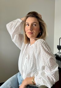 Fehér, textúrált blúz puffos ujjal és apró gombokkal. Világoskék farmerrel párosítva. Egyszerű, klasszikus dizájn, amely lágy megjelenést kölcsönöz.