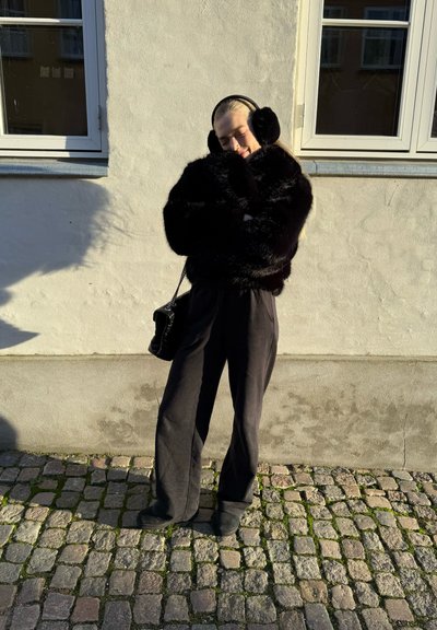 Abrigo negro de piel sintética con mangas anchas, combinado con pantalones negros holgados y un bolso negro texturizado. Textura suave y aterciopelada, y color intenso.