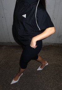 Fekete cipzáras dzseki fehér díszítésekkel, fekete leggings, és hegyes fehér magassarkúk. A hangsúly a hétköznapi városi ruházaton van, letisztult, modern kialakítással.