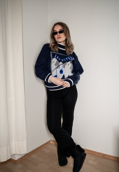 Jersey de punto azul marino con acentos en blanco y azul que presenta un diseño de montaña, combinado con leggings negros y botas negras con forro de piel.