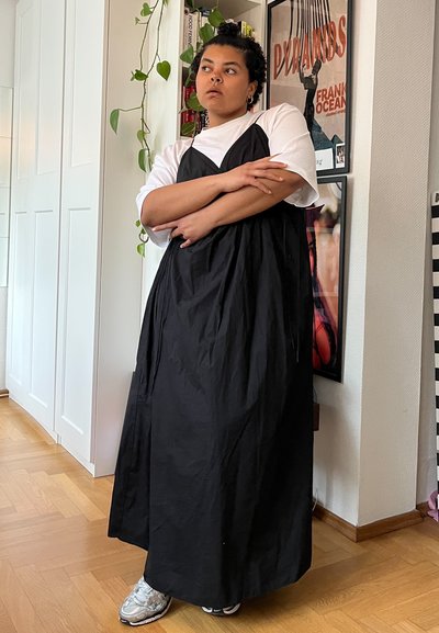 Vestido negro sin mangas con un corte holgado y una textura suave, superpuesto a una camiseta blanca. Combinado con zapatillas plateadas, que muestran un diseño moderno.