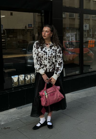 Chaqueta con estampado de vaca en blanco y negro, con cierre lateral y rayas blancas, falda negra, bolso rosa, calcetines blancos y zapatos negros, adornada con accesorios.