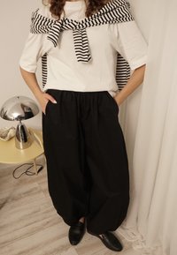 T-shirt en coton blanc associé à un pantalon noir ample, avec une ceinture élastique, et un châle rayé noir et blanc noué autour des épaules.