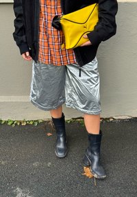 Crna jakna na patentni zatvarač, narančasta i mornarsko plava košulja na kockice, metalik srebrne kratke hlače i crne gležnjače, upareni sa žutom torbicom geometrijskog uzorka.