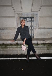Giacca grigia lavorata a maglia con bottoni dorati, pantaloni neri e una borsa a tracolla rosa chiaro con un ciondolo colorato. Collant neri con pois e scarpe nere.