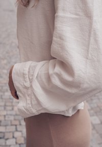 Világos bézs színű, lazán illeszkedő vászon ing, texturált felülettel és felgöngyölített ujjal, amelyet szűk, világos bézs leggings-szel párosítottak.