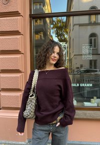 Pull bordeaux à épaules dénudées en matière tricotée douce, associé à un jean gris à jambes larges et un sac à bandoulière à motifs.