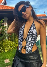 Costume da bagno in stampa zebra bianco e nero con scollatura a V profonda, anelli circolari sul davanti e design a sgambatura alta abbinato a una gonna nera.