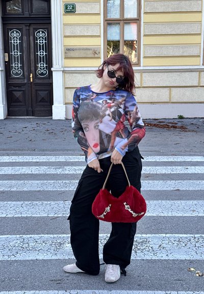 Parte superior de manga larga con un estampado gráfico colorido, pantalones cargo negros y un bolso de piel sintética rojo con acentos plateados. Zapatillas blancas.