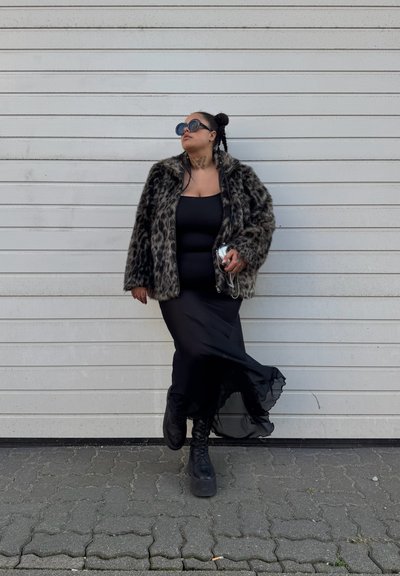 Abrigo de piel sintética con estampado de leopardo, vestido negro ajustado, falda negra fluida y botas de plataforma negras gruesas. Los accesorios incluyen gafas de sol redondas.