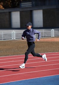 Kvinde i træningstøj og kasket sprintende på en udendørs løbebane i klart sollys.