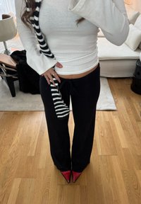 Haut blanc à manches longues côtelé associé à un pantalon noir à jambes larges. Accessoire rayé noir et blanc. Chaussures rouges à bout pointu.