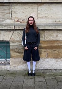 Pessoa a usar um suéter gola alta cinza escuro, calças culottes de denim preto, meias brancas até a coxa e sapatos plataforma pretos chunky, com uma bolsa branca.