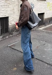 Barna bomber dzseki, kék bő szárú farmernadrág, és egy fekete szőtt kézitáska. A dzsekin egy folt található az ujjon, a táskának pedig sima textúrája van.
