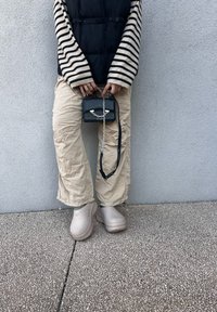 Ελαφρύ, μπεζ ρυτιδωτό παντελόνι, μαύρο και λευκό ριγέ μπλούζα με μακριά μανίκια, γιλέκο puff, γκρίζες παντόφλες και μικρή μαύρη τσάντα χεριού με ασημένια αξεσουάρ.