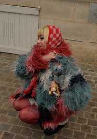 Wielokolorowy, puszysty płaszcz o szorstkiej fakturze. Czerwona i biała kraciasta kaptur, warstwowe ubrania, dodatki oraz zabawny styl.