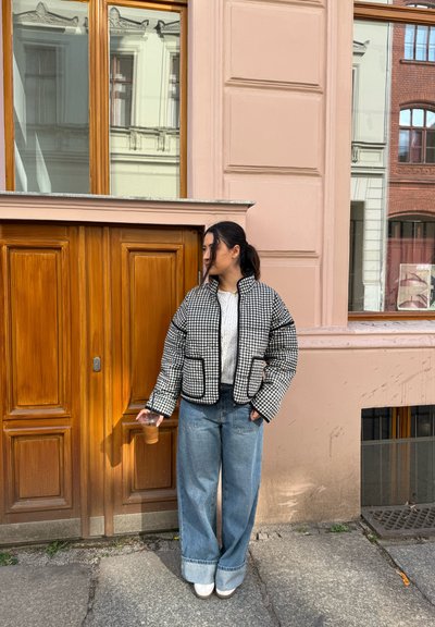 Chaqueta acolchada de cuadros en blanco y negro con ribetes en negro, combinada con jeans de tiro alto en un azul claro de perneras anchas y zapatos blancos.