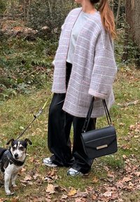 Cardigan à carreaux rose clair et gris avec de larges manches, haut gris, pantalon noir et sac à main noir avec un accent doré. Petit chien en laisse.