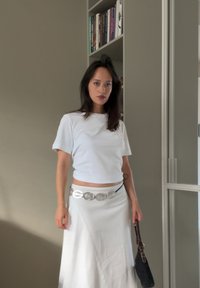 Witte aansluitende t-shirt met korte mouwen, gecombineerd met een vloeiende witte rok, vastgemaakt met een grote zilveren riem, en een kleine zwarte handtas.