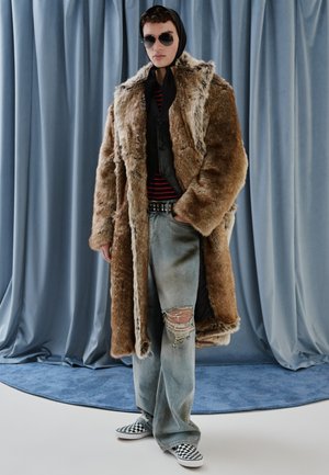 Lažno krzneni plašč v rjavi barvi, položen čez črn brezrokavnik in črtasto srajco. Uporabljen z unikatnimi svetlo modrimi džinsom in črno-belim karirastim natikačem.