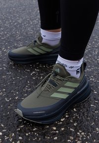 Chaussures de sport vertes avec une tige texturée, rehaussées de bandes noires et vert clair. Dotées d'une semelle coussinée et de lacets réglables.