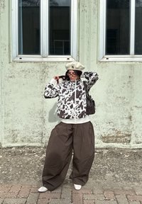 Croppet genser med svart og hvitt ku-mønster, kombinert med løse brune bukser. Et kremfarget beret fullfører antrekket, sammen med hvite sko.