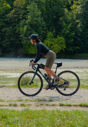 Bicicleta con un marco negro y neumáticos delgados, con un diseño aerodinámico. El ciclista lleva una camiseta de manga larga negra, pantalones cortos de color oliva y un casco.